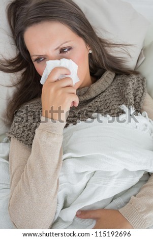 Sick woman holding tissue to nose on the couch