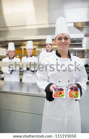 Chef presenting her salads in kitchen with team behind her