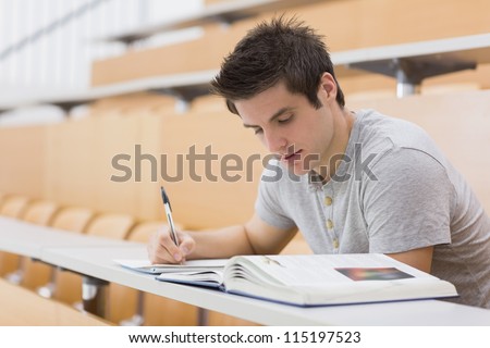 Student sitting reading a book and taking notes in lecture hall