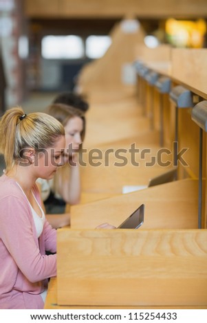 Woman sitting at study desks studying with tablet pc in college library