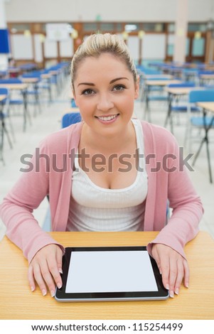 Woman sitting holding tablet pc smiling in empty exam hall in college