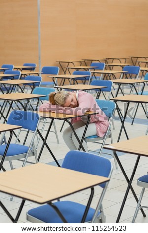 Student leaning on desk napping in exam hall of college