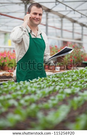 Smiling man on the phone and taking notes in greenhouse in garden center