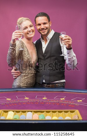Two people standing at table in a casino while amusing and toasting