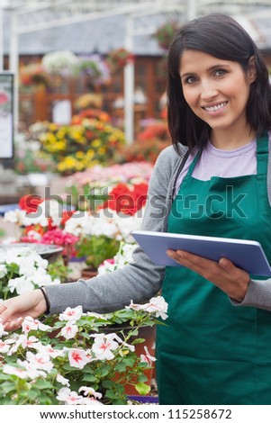 Smiling worker checking flowers in garden center with tablet computer
