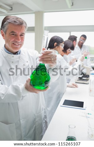 Chemist holding beaker of green liquid in busy lab