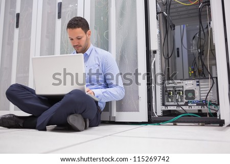 Man sitting on floor with laptop beside servers in data center