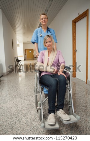 Nurse puching wheelchair of patient with arm sling in hospital corridor