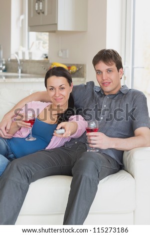 Young couple sitting on the couch while watching television and drinking wine