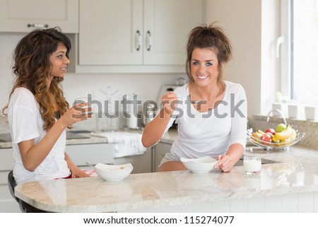 Two friends eating bowls of cereal while standing in a kitchen