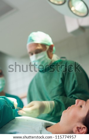 Patient sleeping on a surgical table while a surgeon is taking scissors in a surgical room