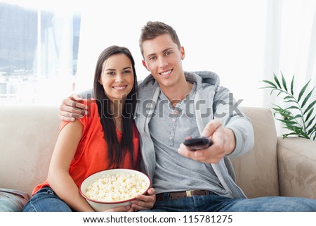 A smiling couple holding each other as they change the channel and look into the camera