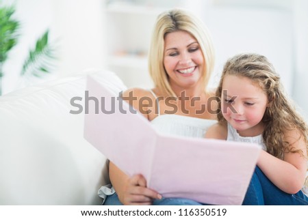 Mother with her daughter reading book on the sofa