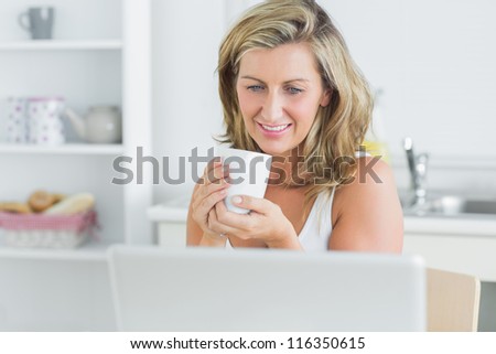 Smiling woman holding mug in kitchen with laptop