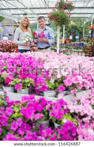 Couple standing in garden center holding potted plants