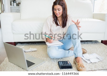 Woman working out finances with laptop on floor of living room
