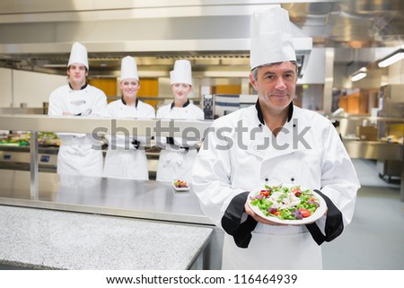 Head chef presenting salad with his team standing behind him