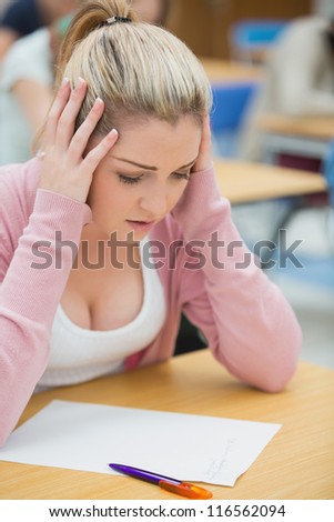 Student looking at exam paper and stressing in exam hall