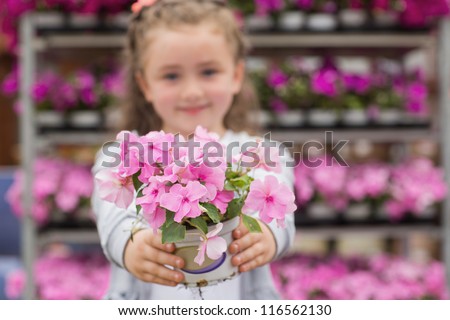Little girl holding pink flowers out in garden center