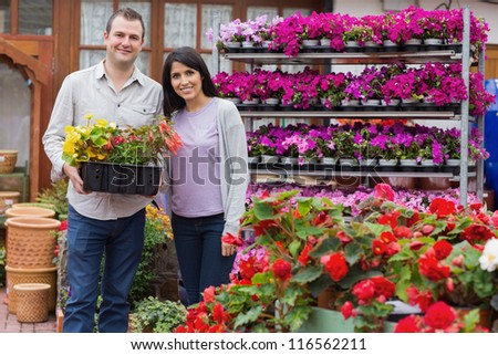Happy couple holding tray of plants in garden center