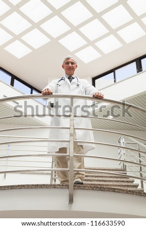 Doctor standing an the railing at the corridor of the hospital looking down