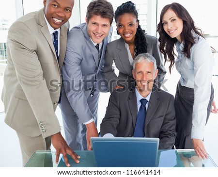 Mature businessman sitting at the desk surrounded by his smiling team