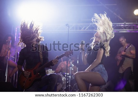 Female singer and male guitarist with tousled hair performing together on stage at nightclub