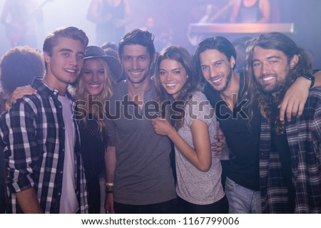Portrait of smiling friends with arm around standing in nightclub