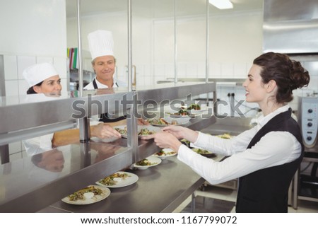 Chef handing food dish to waitress at order station in the commercial kitchen