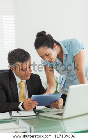 Man and woman working together on a digital tablet and a laptop in an office