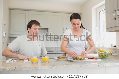 Two people are in the kitchen while one of them makes sandwiches