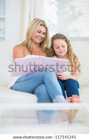Smiling mother and daughter while reading book on couch
