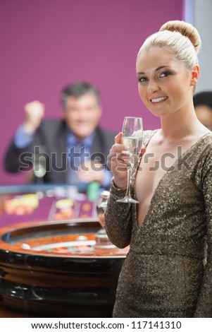 Woman with champagne standing beside roulette wheel as man is cheering behind her