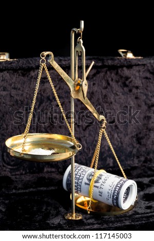 Weighing scales comparing wad of dollars and pile of white illegal drug