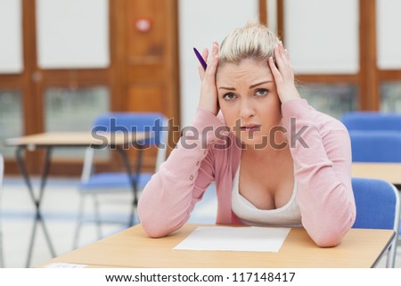 Woman looking worried over exam paper in exam hall in college