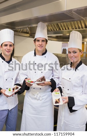 Three happy Chef\'s presenting cakes in the kitchen