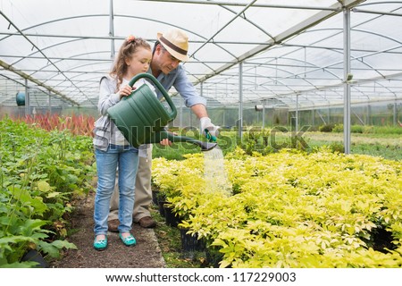 Gardener and granddaughter watering plants in greenhouse