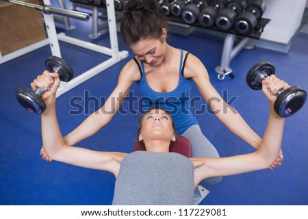 Cheerful trainer helping woman lifting weights in gym