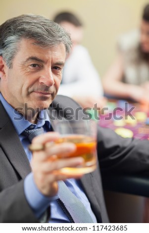 Man lifting glass of whiskey at roulette table in casino