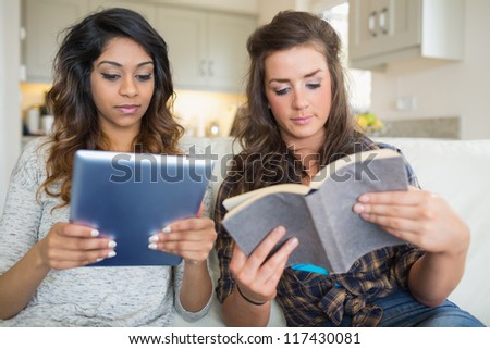 Girls reading a book and holding a tablet computer while sitting on a couch