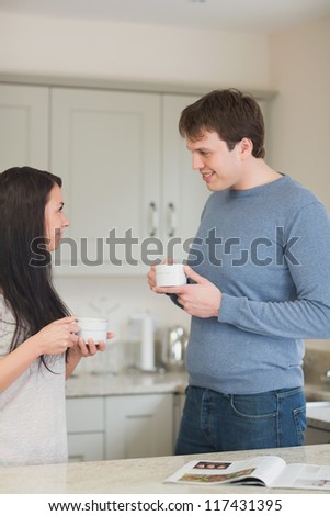 Two people standing in the kitchen and drinking coffee while talking