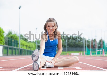 Cheerful woman stretching her leg on a track
