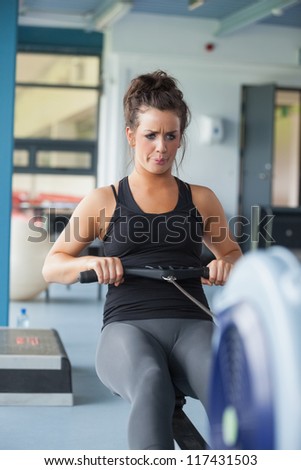 Exhausted woman training on row machine in gym