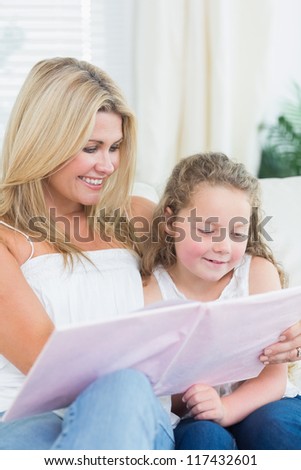 Smiling mother and daughter sitting on the sofa with a book