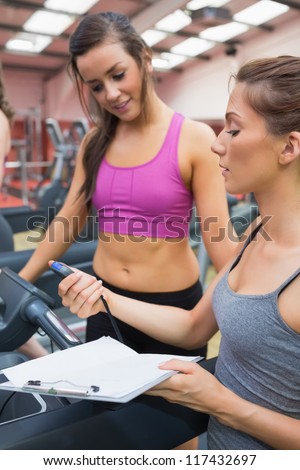 Female trainer showing client her time on treadmill in gym