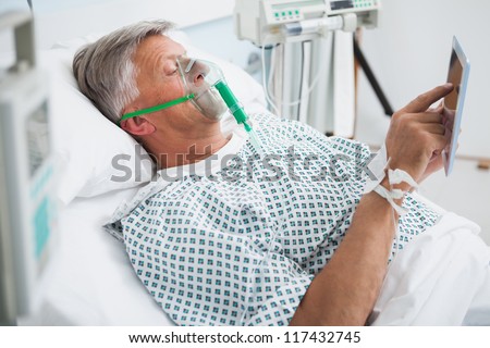Patient is lying in bed reading wearing an oxygen mask in hospital ward