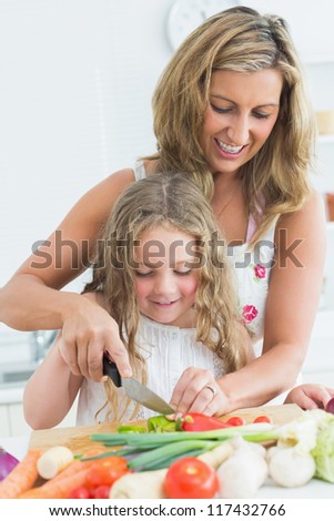 Smiling mother teaching her daughter cutting various vegetables