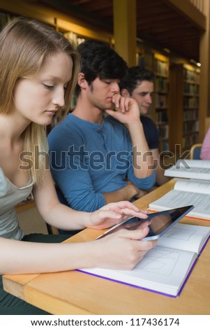 Woman in study group using tablet pc at desk in college library