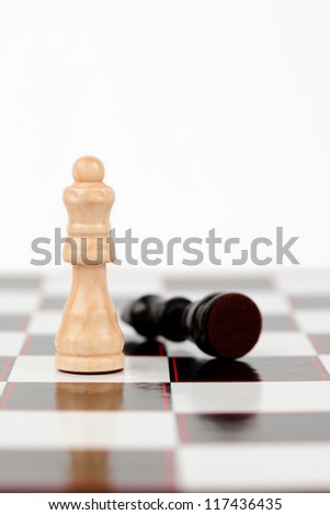 White queen standing with black queen lying at the chessboard