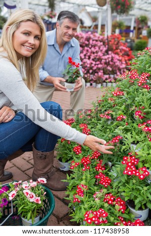 Couple crouching to look at red flowers in garden center